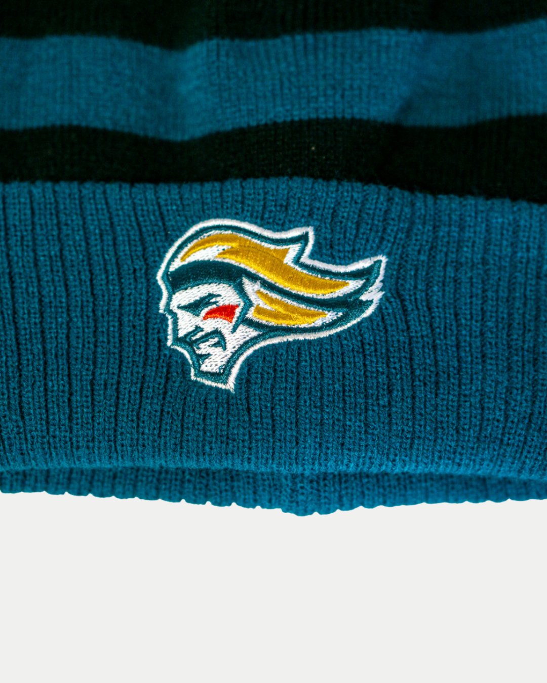 Close-up of the Belfast Giants Hockey Beanie Striped Black by Belfast Giants, featuring teal and black stripes and an embroidered face logo—a must-have cold-weather essential.