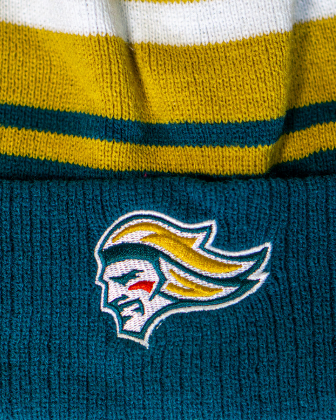 Close-up of the Belfast Giants Hockey Beanie Striped Gold by Belfast Giants, featuring yellow and white bands, a green cuff, and an embroidered logo of a stylized face—an ideal winter hat for fans.