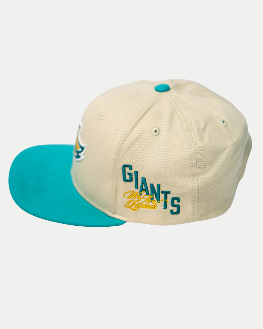 The Belfast Giants Hockey Cap Off-White by Belfast Giants features a teal brim, blue-and-yellow "GIANTS" side embroidery with cursive text below, and is adjustable. Presented against a white background.