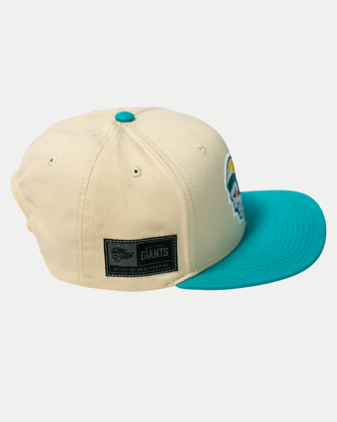 The Belfast Giants Hockey Cap Off-White by Belfast Giants has a teal brim and button, a GIANTS side patch, and an embroidered front logo. This adjustable cap is shown on a white background.