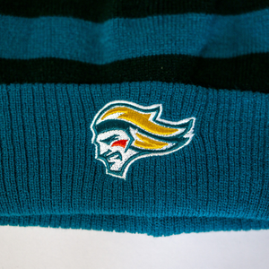 A close-up of the Belfast Giants Hockey Beanie Striped Black, a cozy teal knit hat by Belfast Giants, features an embroidered stylized head with yellow hair and a red cheek mark against dark green horizontal stripes.