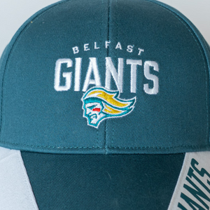The Belfast Giants Cap Teal and White Brim by Belfast Giants features embroidered “Belfast Giants” text and a stylized head logo with yellow hair, a teal face, and red markings.