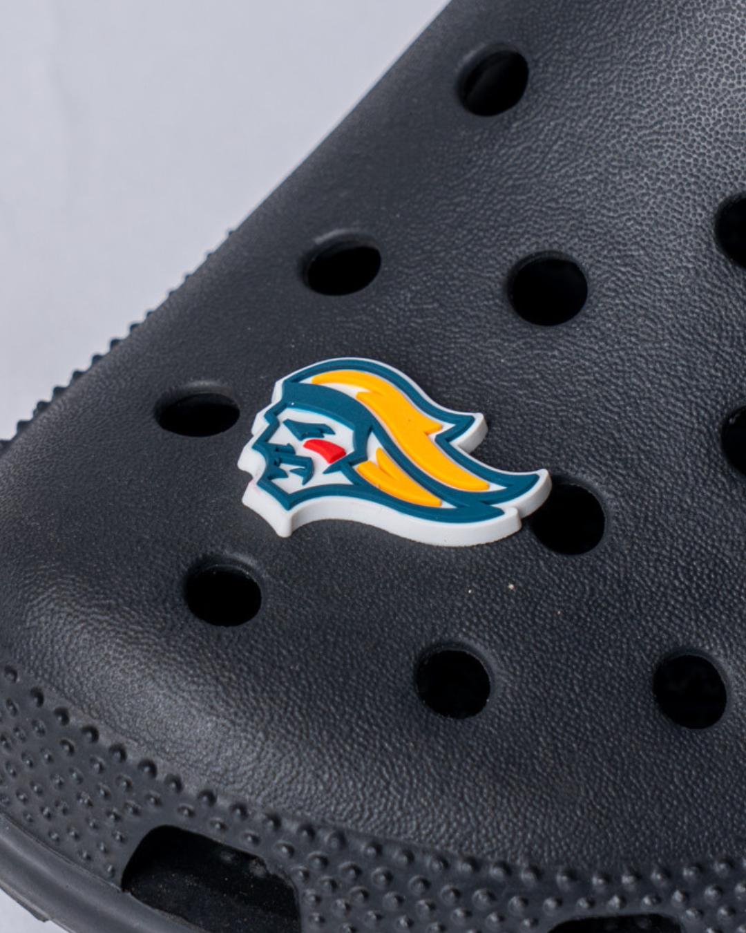 A close-up of a black perforated clog shoe with a Belfast Giant Croc Charm featuring the Belfast Giants warrior logo in yellow hair and blue helmet, available from Belfast Giants Store by National Merchandise.