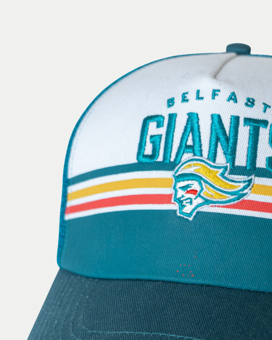 A close-up of the Belfast Giants Cap Teal/White Peak by Belfast Giants, showing "BELFAST GIANTS" above a stylized giant’s head and horizontal yellow, orange, and red stripes.