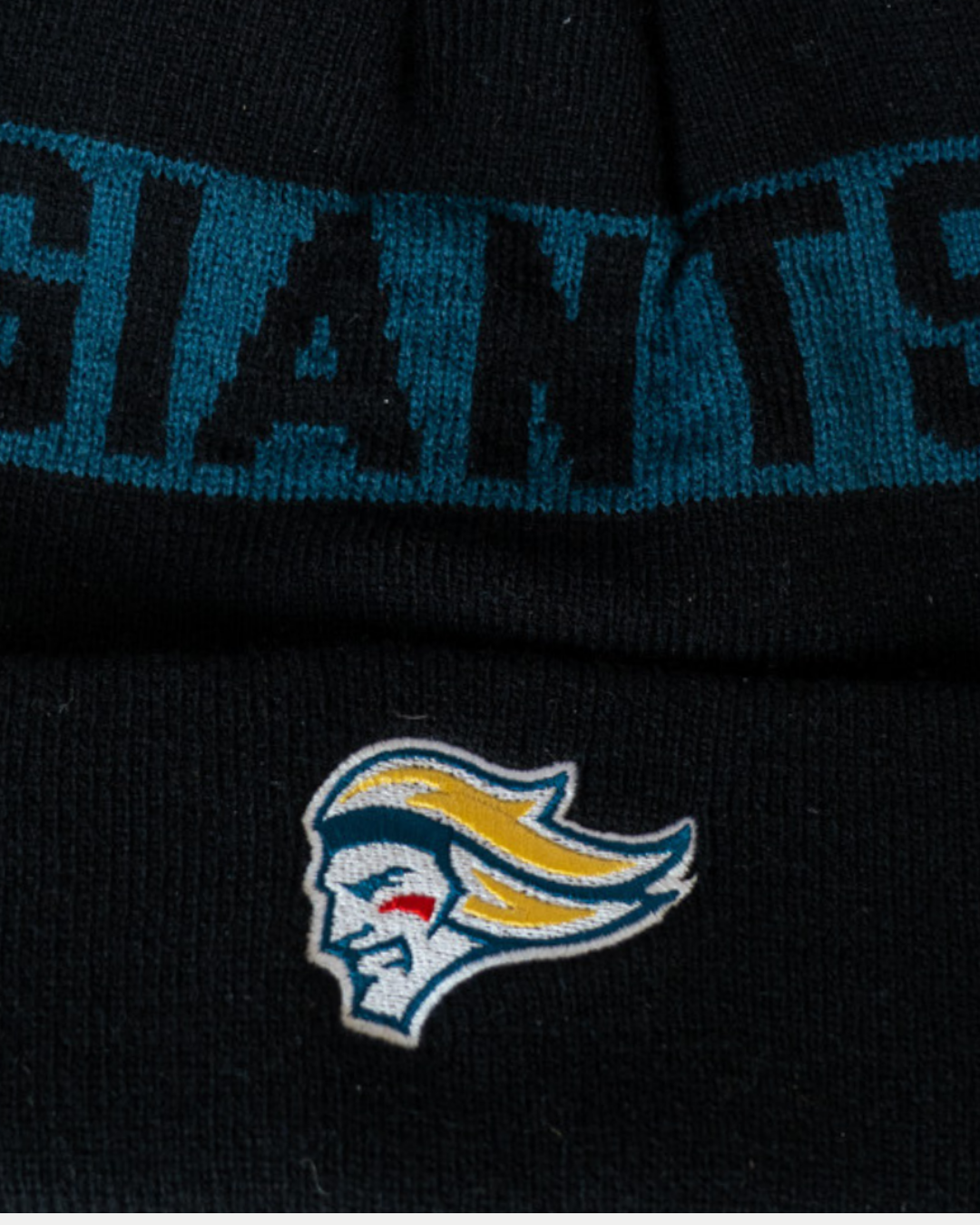 A close-up of the Belfast Giants Black Beanie Head Logo by Belfast Giants, featuring bold "GIANTS" lettering and an embroidered stylized head logo with yellow hair and blue accents.