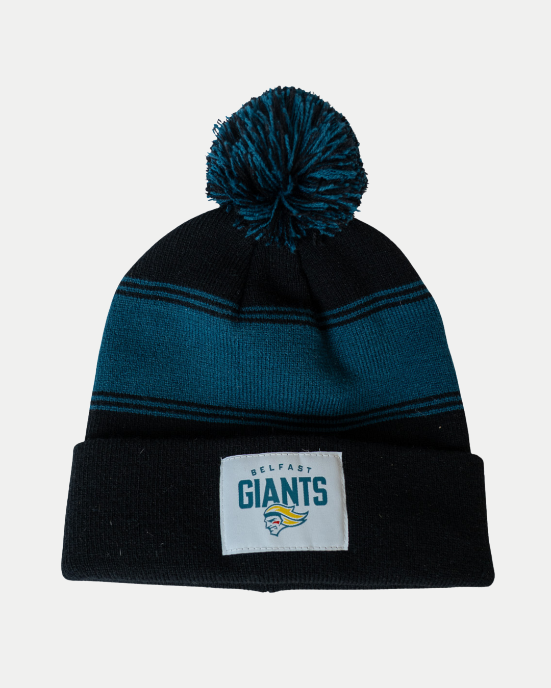 The Belfast Giants Black Beanie Teal Stripes features bold teal stripes, a pom-pom top, and the official Belfast Giants logo patch embroidered on the front cuff.