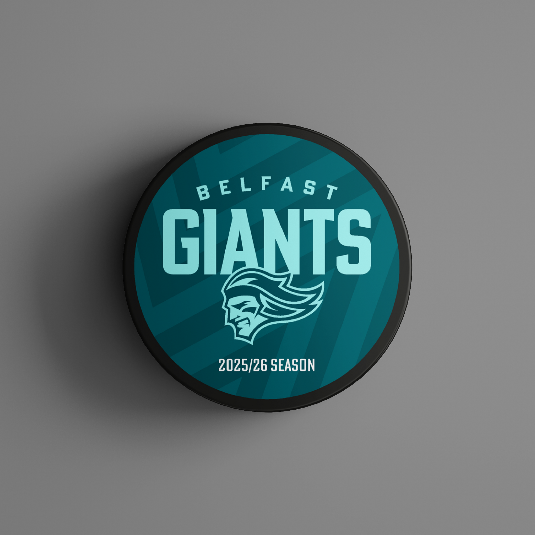 The Logo Season Puck Text 25-26 from Belfast Giants Store by National Merchandise is a teal ice hockey puck with Belfast Giants, a giant head logo, and 2025/26 Season on a chevron-patterned background.