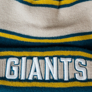 A close-up of the Belfast Giants Beanie Cream/Teal, a knitted hat with blue, yellow, and white stripes and “GIANTS” embroidered in large white letters. Brand: Belfast Giants.