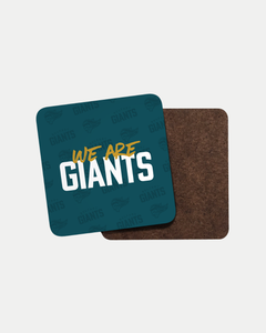 The We Are Giants Coaster by Belfast Giants features a blue top with bold "WE ARE GIANTS" text and a subtle repeating GIANTS logo pattern. Made-to-order to reduce waste, with another plain brown coaster partially visible behind it.