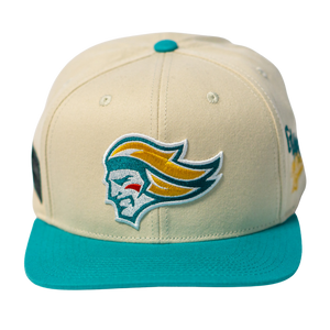 The Belfast Giants Hockey Cap Off-White by Belfast Giants is an off-white adjustable hat with a teal brim and features a yellow and teal embroidered stylized knight’s head logo on the front.