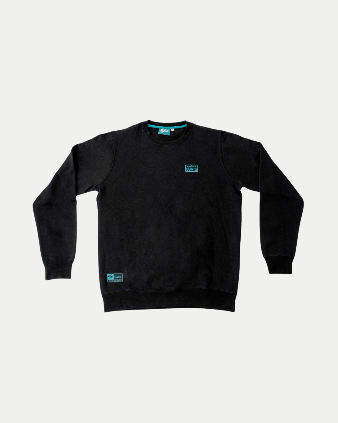 The Belfast Giants Black Sweatshirt Teal Badge features long sleeves and two small teal and white rectangular logo patches—one on the chest, one near the bottom hem—shown on a clean white background.