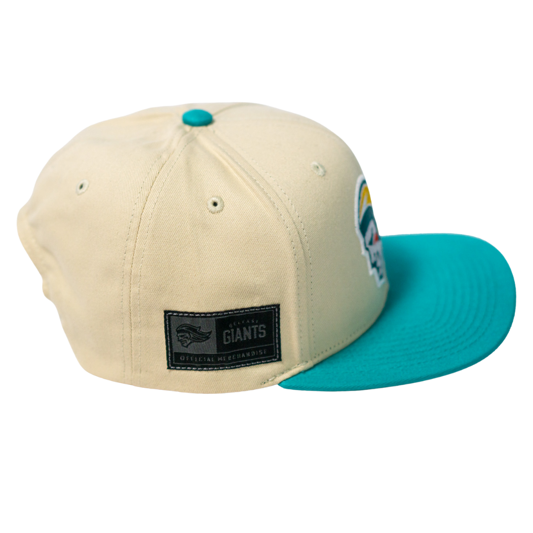 The Belfast Giants Hockey Cap Off-White features a teal brim and button, a Giants Official Merchandise patch, and a colorful side logo. This adjustable Belfast Giants hat is shown on a transparent background.