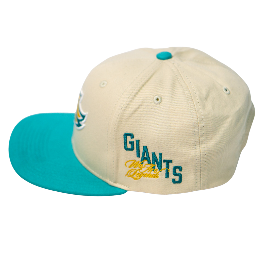The Belfast Giants Hockey Cap Off-White by Belfast Giants is an adjustable off-white hat with a teal brim and button, featuring GIANTS embroidered in teal and gold script on the side.
