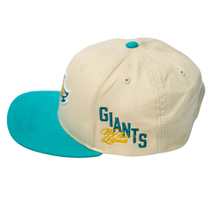 The Belfast Giants Hockey Cap Off-White by Belfast Giants is an adjustable off-white hat with a teal brim and button, featuring GIANTS embroidered in teal and gold script on the side.