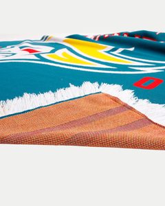 A close-up of the Belfast Giants Blanket by Belfast Giants, featuring a colorful blue, white, yellow, and red jacquard pattern on one side, an orange and brown plaid reverse, and finished with a white fringed edge.
