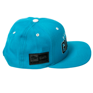 The Belfast Giants Teal Snapback Cap features white eyelets, a flat brim, an OFFICIAL MERCHANDISE side patch, and a partially visible GIANTS team crest on the front.