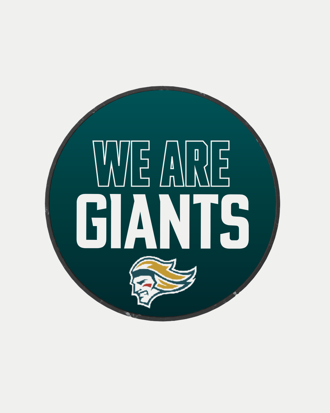 The We Are Giants Logo Puck 25-26 from Belfast Giants Store features a circular dark teal design with "WE ARE GIANTS" in bold white letters above a mascot logo, showcasing yellow and green hair accents.