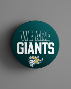 A round teal puck featuring "WE ARE GIANTS" in white text above a stylized giants head logo, from the Belfast Giants Store by National Merchandise. Product: We Are Giants Logo Puck 25-26. Background is gray.