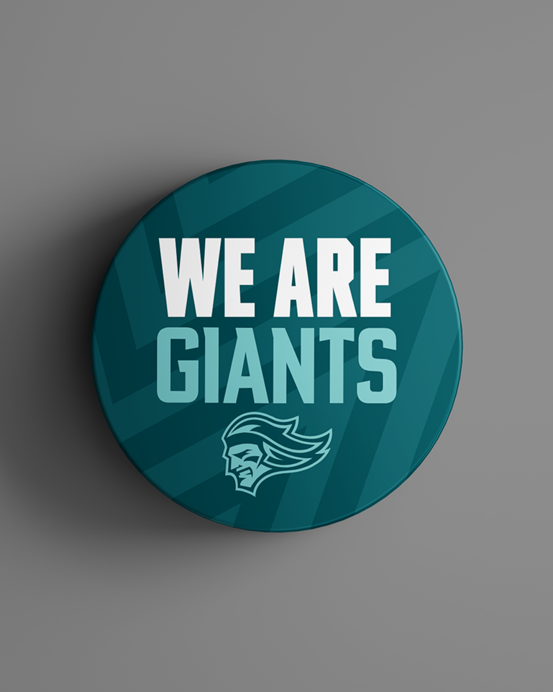 The We Are Giants Teal Logo Puck 25-26 from Belfast Giants Store by National Merchandise features bold white and light blue text above a mascot head on a striped background.