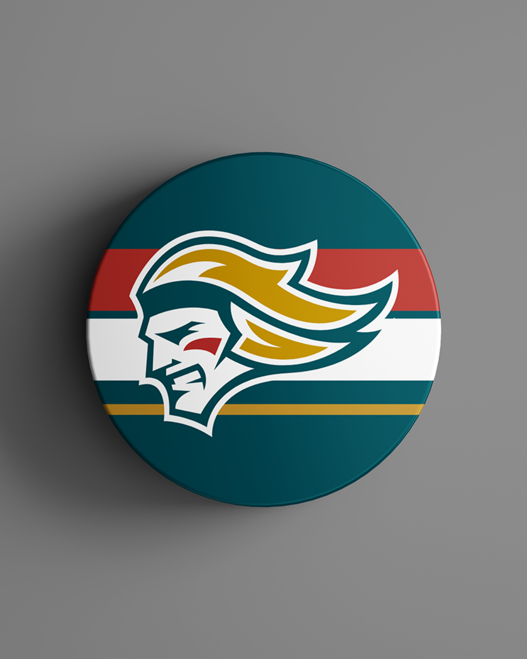 The Belfast Giants Striped Hockey Puck 25-26 from the Belfast Giants Store by National Merchandise features a round badge with a stylized knight's head in teal, gold, and white over red, white, teal, and gold stripes on a gray background.