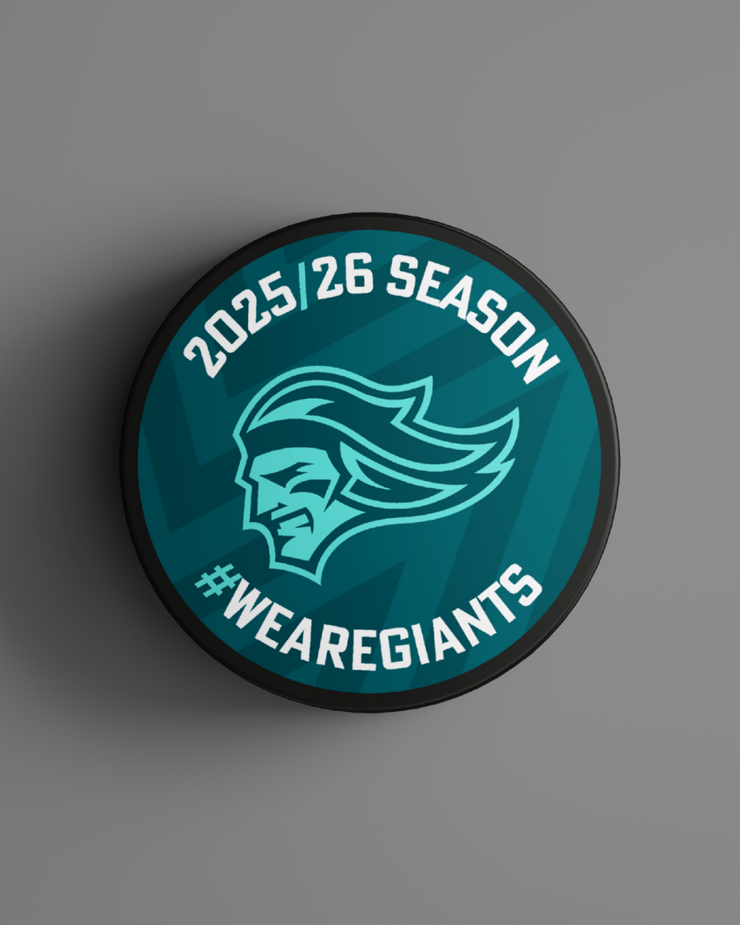 The Logo Season Puck Teal 25-26 by Belfast Giants Store features a stylized head logo, "2025|26 SEASON" at the top, and "#WEAREGIANTS" at the bottom on a teal puck against a gray background.