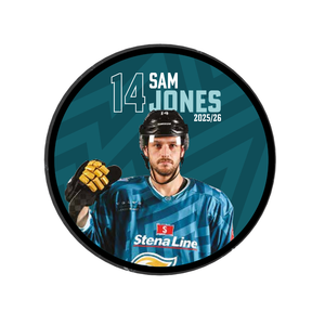 A male ice hockey player in blue gear and helmet stands holding his stick. The circular 2025-26 Player Puck features Belfast Giants branding, number 14 Sam Jones, Stena Line on the jersey, and is a striking limited edition tribute.