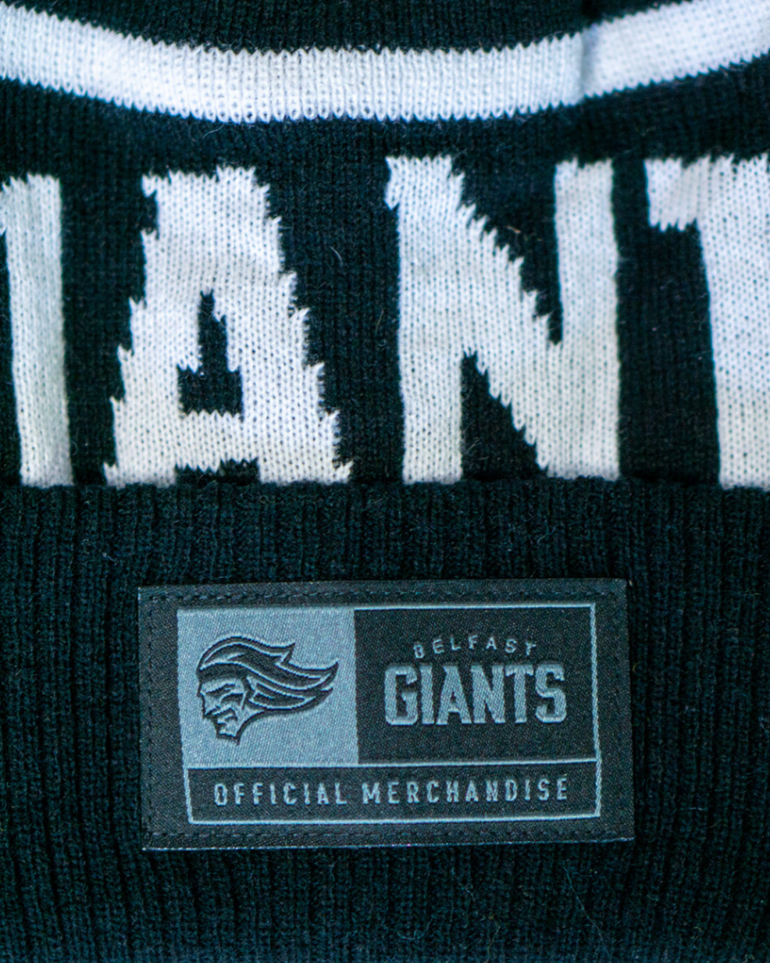 A close-up of the Belfast Giants Beanie Black and White shows a stitched label with the Belfast Giants logo and "Official Merchandise," making this stylish hat ideal for fans.