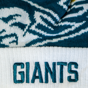 A close-up of the Belfast Giants Hockey Beanie Off-White by Belfast Giants, featuring GIANTS embroidered in green on a white band with a blue and white graphic pattern—ideal for winter matchdays.