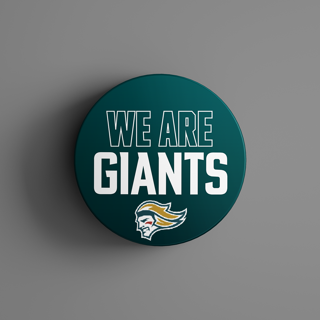 The We Are Giants Logo Puck 25-26 from Belfast Giants Store by National Merchandise features bold white WE ARE GIANTS text and a stylized helmeted mascot head on a round, dark teal background.